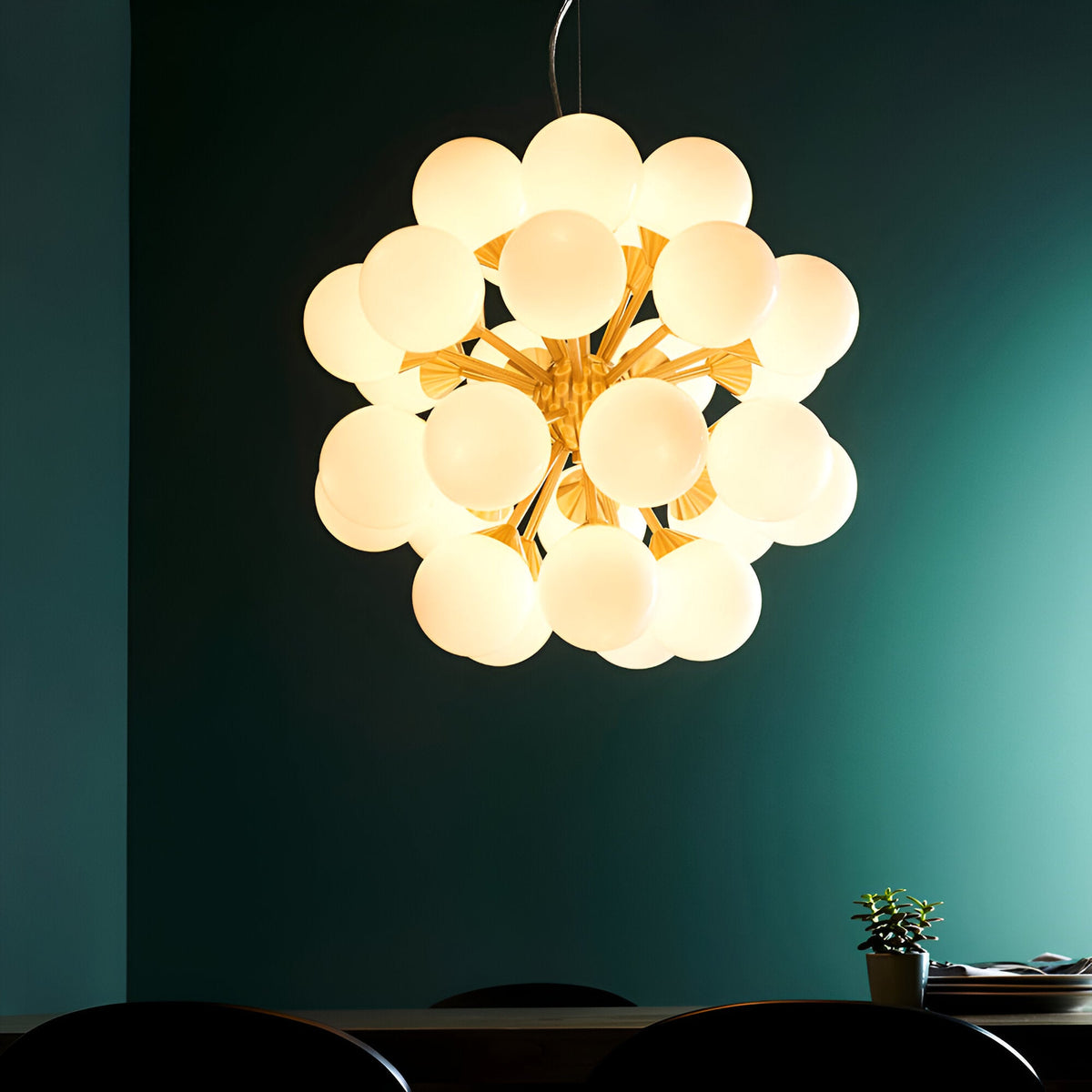 Fitzroy 28 Light Pendant in brushed brass with clustered white opal glass globes, hung above a dining table against a dark teal wall.
