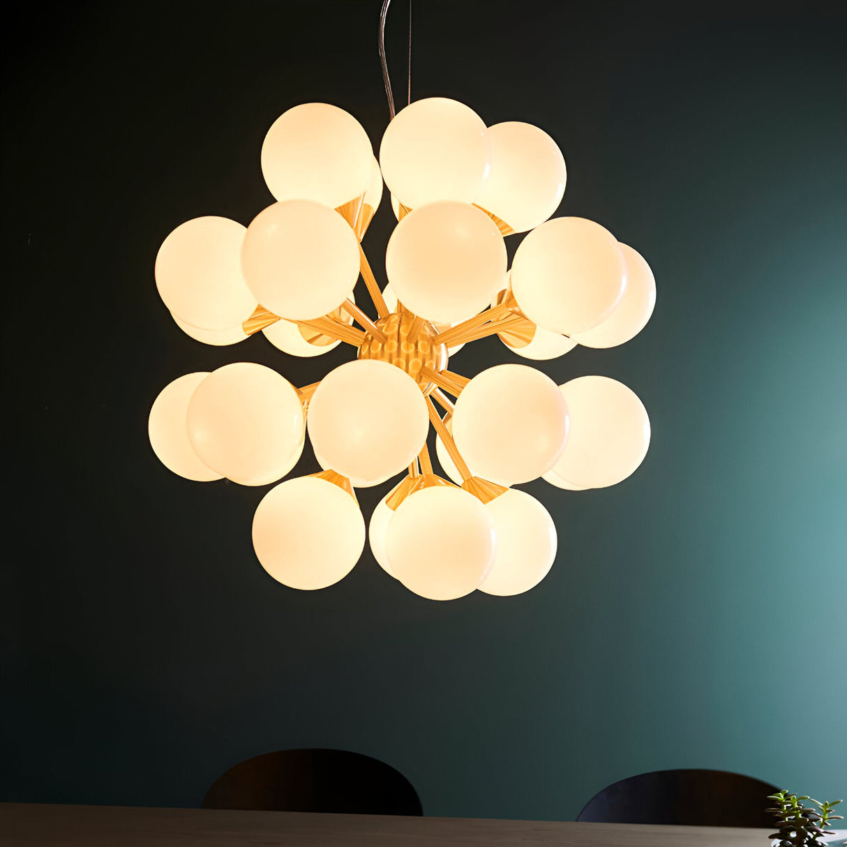 Fitzroy 28 Light Pendant in brushed brass with clustered white opal glass globe shades, hung above a dining table against a dark teal wall.