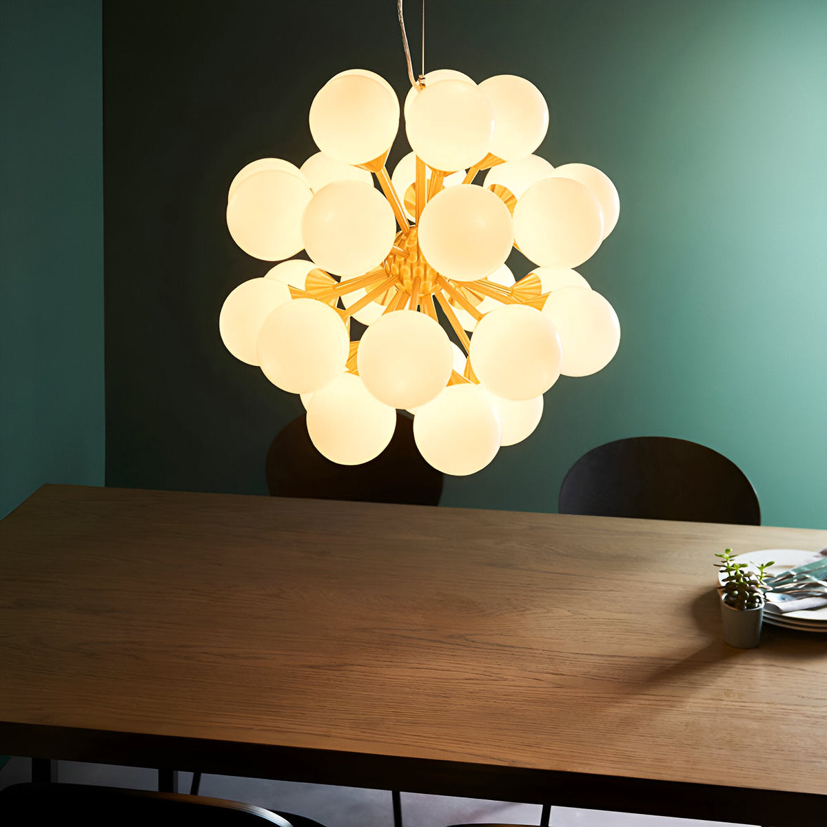 Fitzroy 28 Light Pendant in brushed brass with clustered white opal glass globe shades, hanging above a wooden dining table in a teal-walled room.