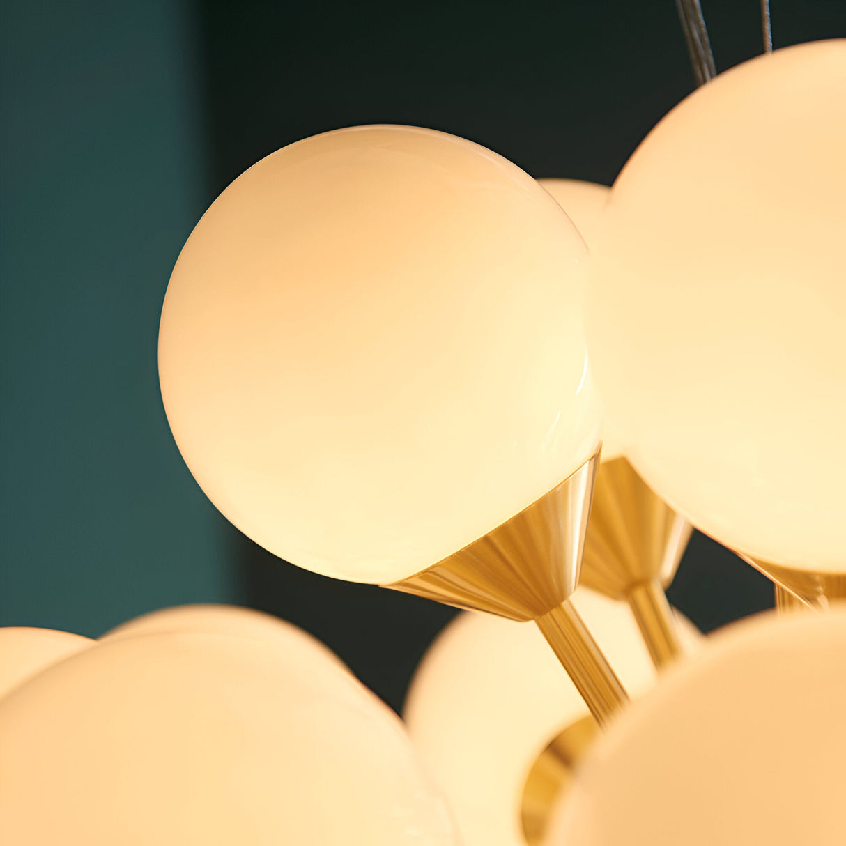 Fitzroy 28 Light Pendant close-up showing round opal glass globe shades on brushed brass fittings against a dark teal background.