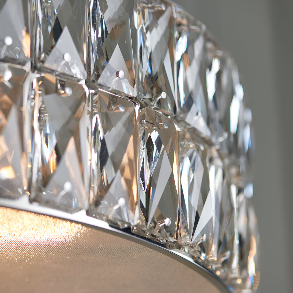 Close-up of the Marguerite LED round pendant in chrome, showing faceted crystal panels and a fabric diffuser with warm light glowing through.