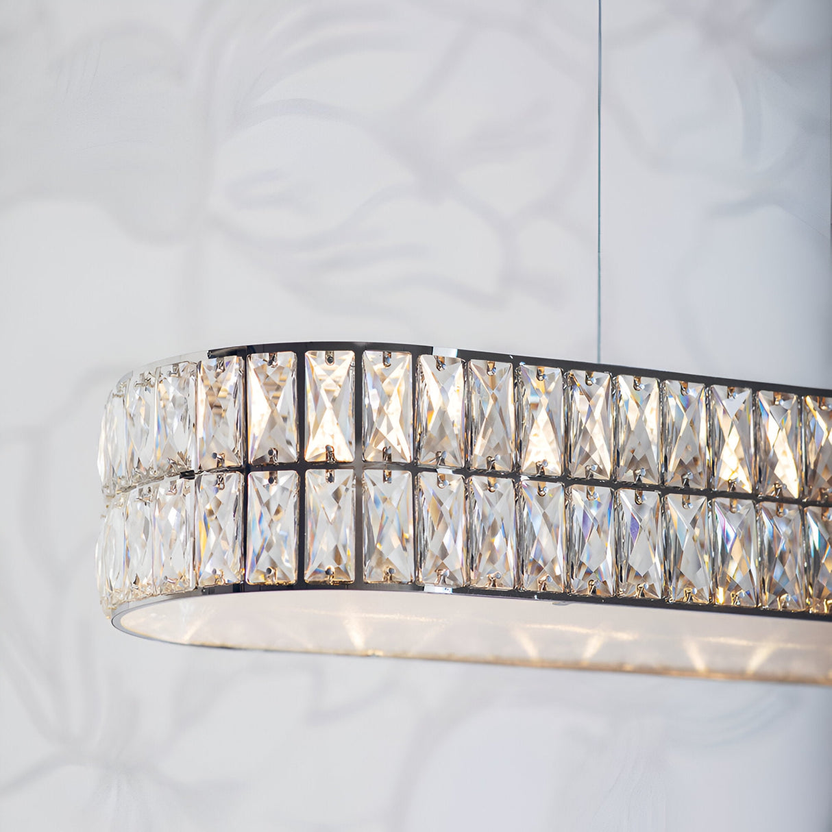 Endon Marguerite linear pendant in polished chrome with two rows of faceted crystals and a prismatic glass diffuser, shown lit against a light wall.