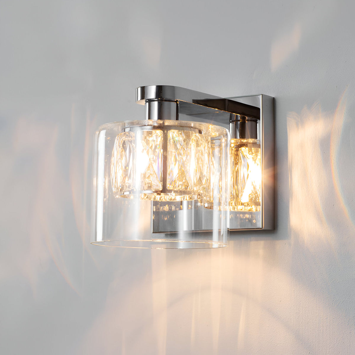 Endon Marguerite chrome wall light with faceted crystal shade inside a clear glass diffuser, illuminated against a plain pale wall.