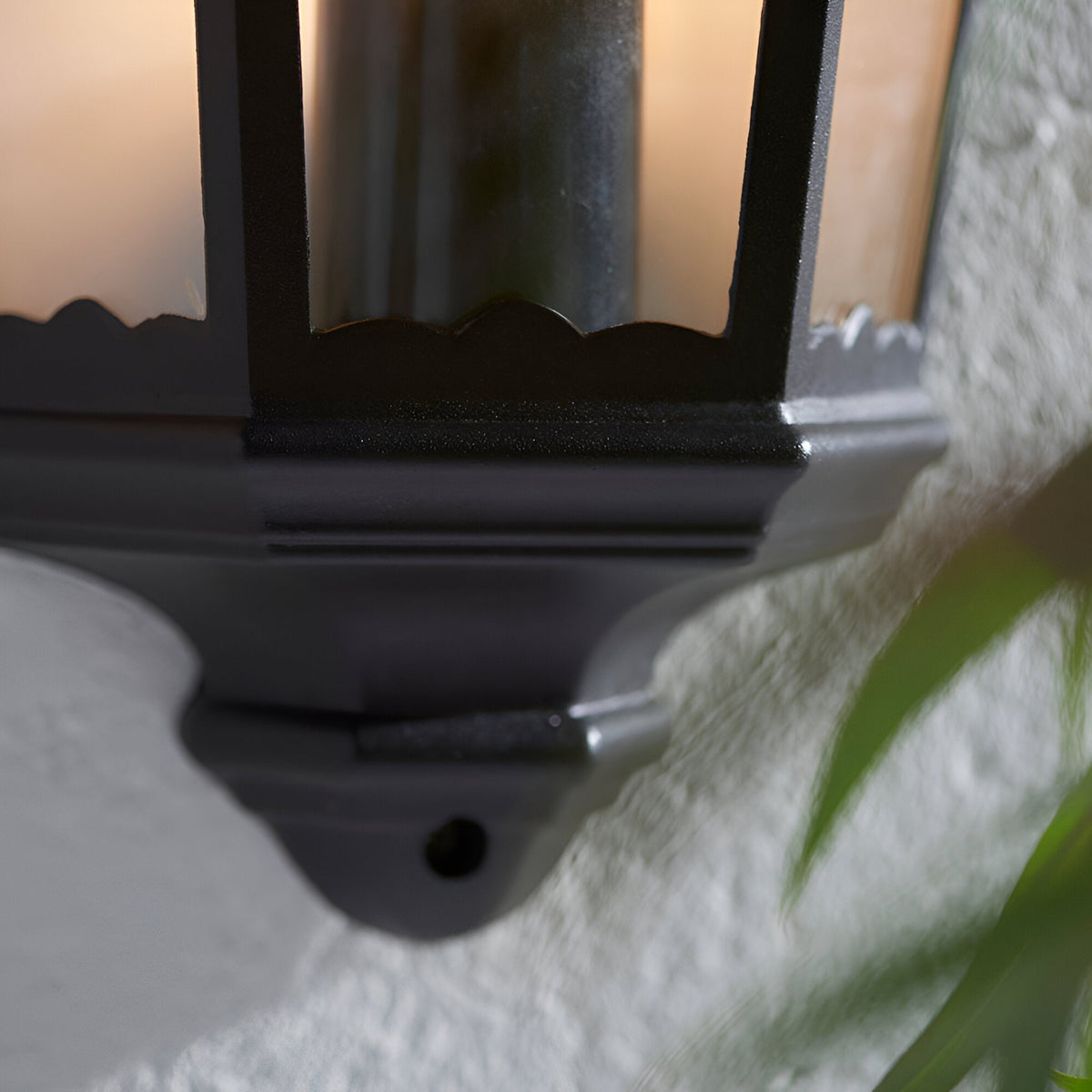 Close-up of the Ashshaw Coach Lantern wall light in matt black die-cast aluminium with clear glass panels, mounted against a textured white wall.