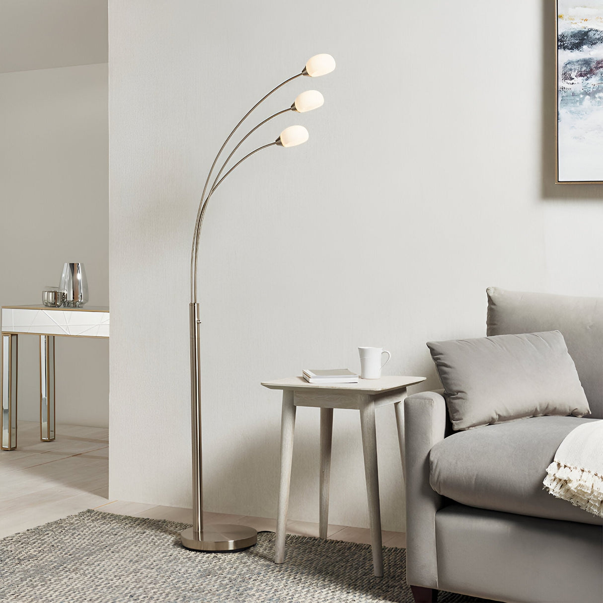 Endon Brockcombe 3 light floor lamp in satin nickel with white glass shades on arched arms, beside a side table and grey sofa in a living room.