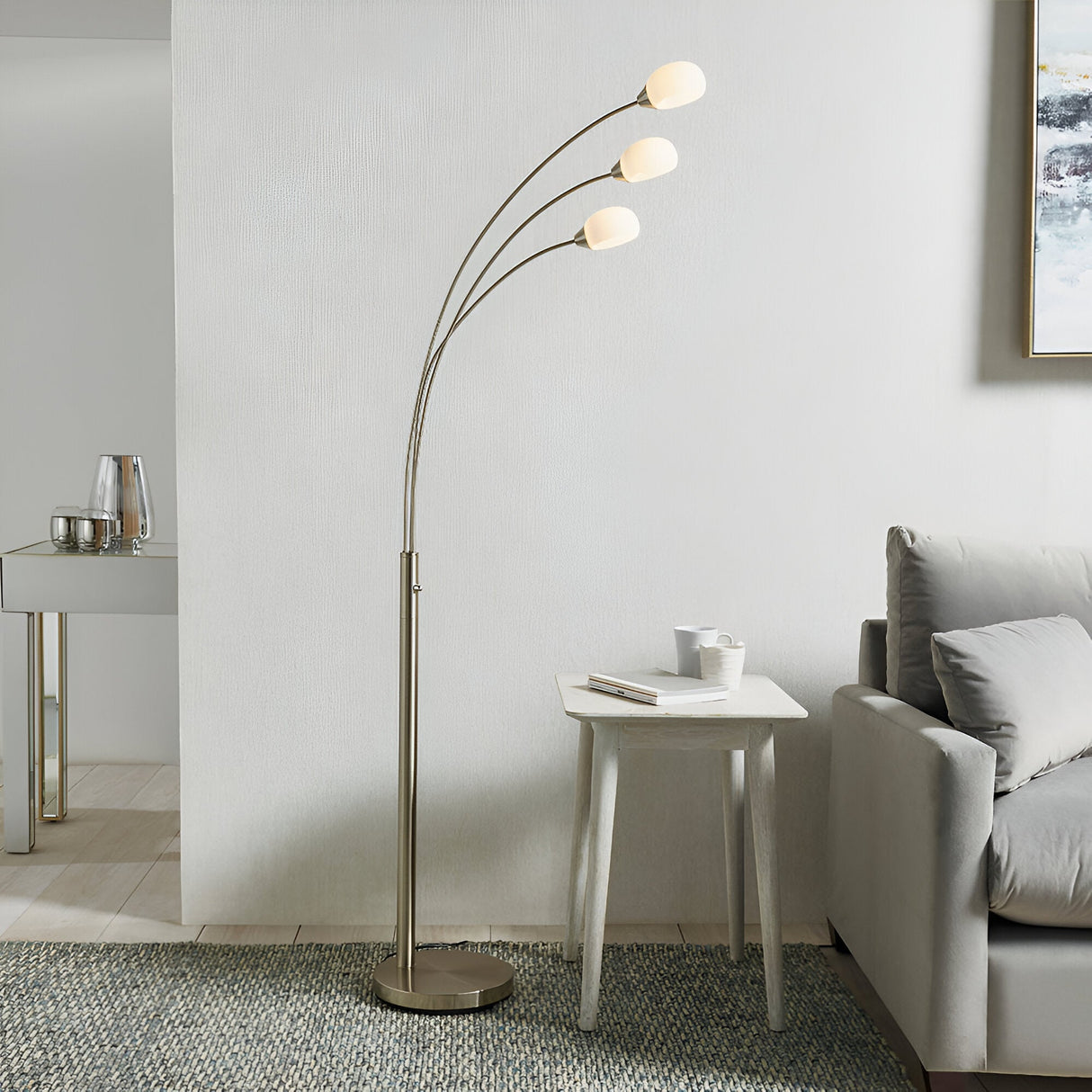 Endon Brockcombe 3 light floor lamp in satin nickel with white glass shades on arched arms, beside a sofa and side table in a modern living room.