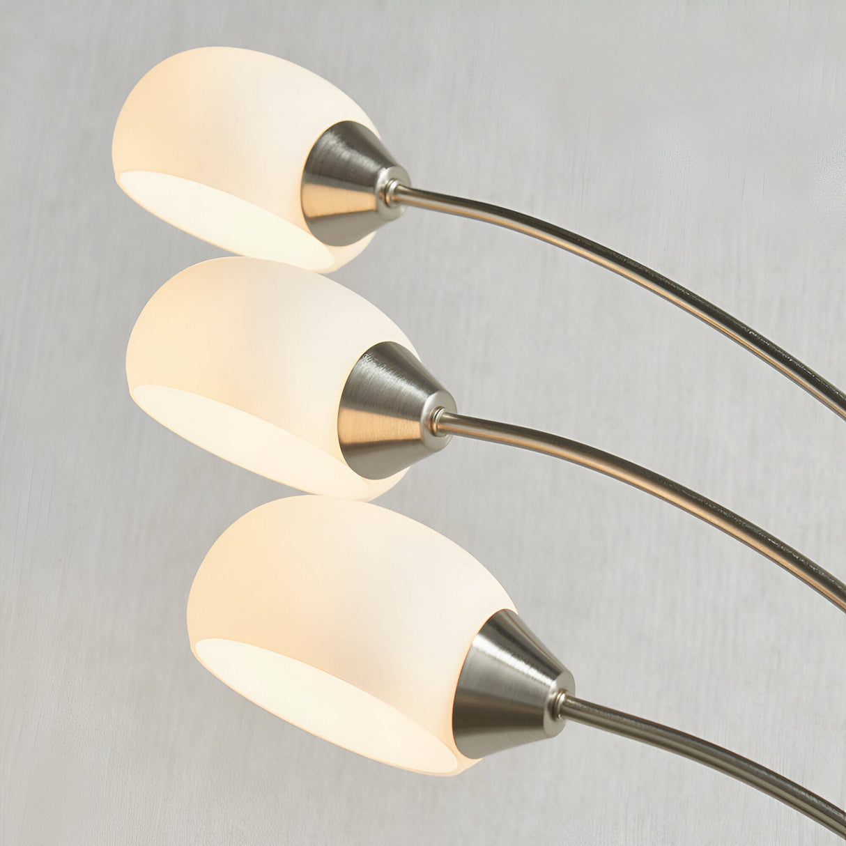 Close-up of Endon Brockcombe 3 Light Floor Lamp in satin nickel, showing three white glass shades on arched arms against a light grey background.