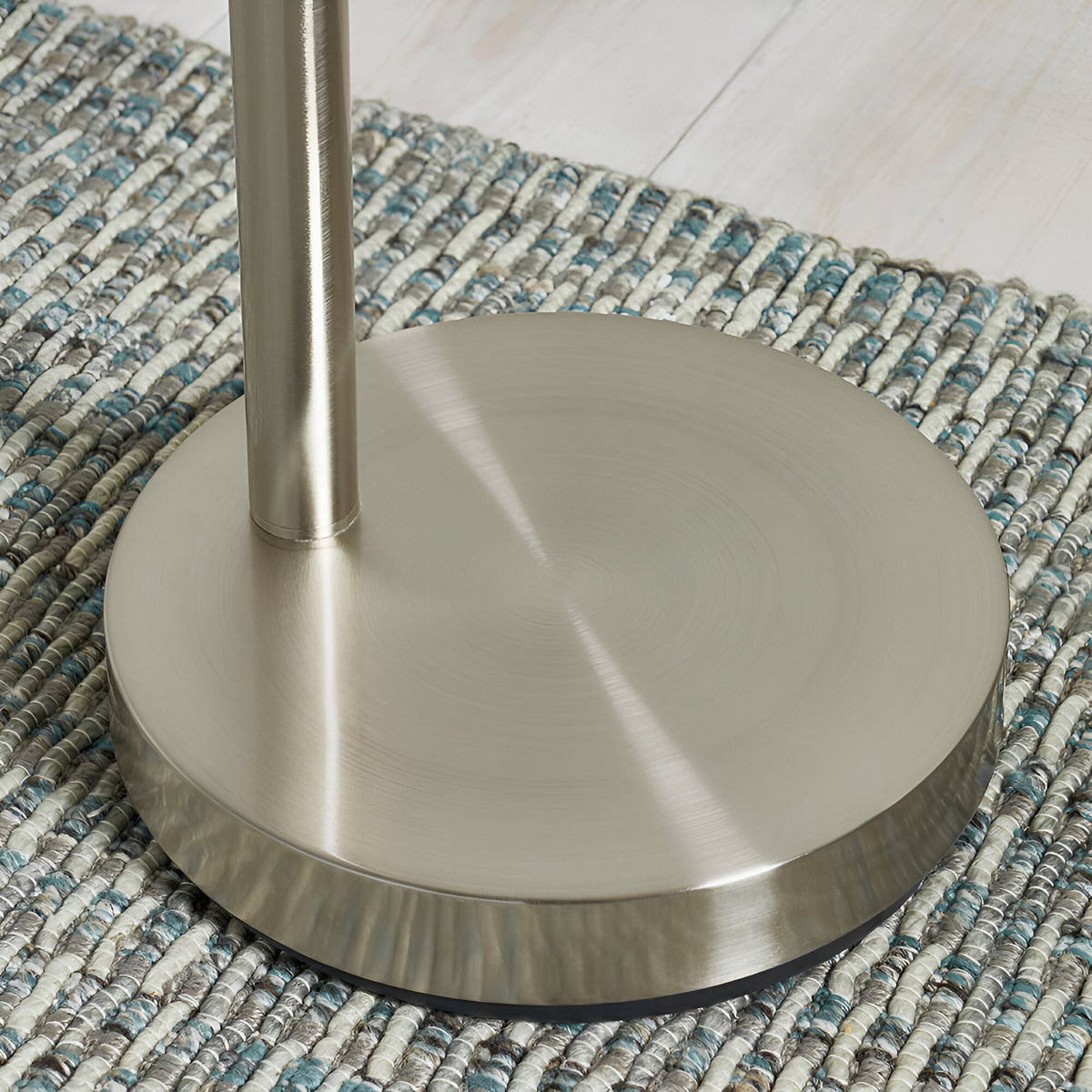 Close-up of the Brockcombe 5 Light Floor Lamp's round satin nickel base and pole, shown on a woven blue and grey rug.