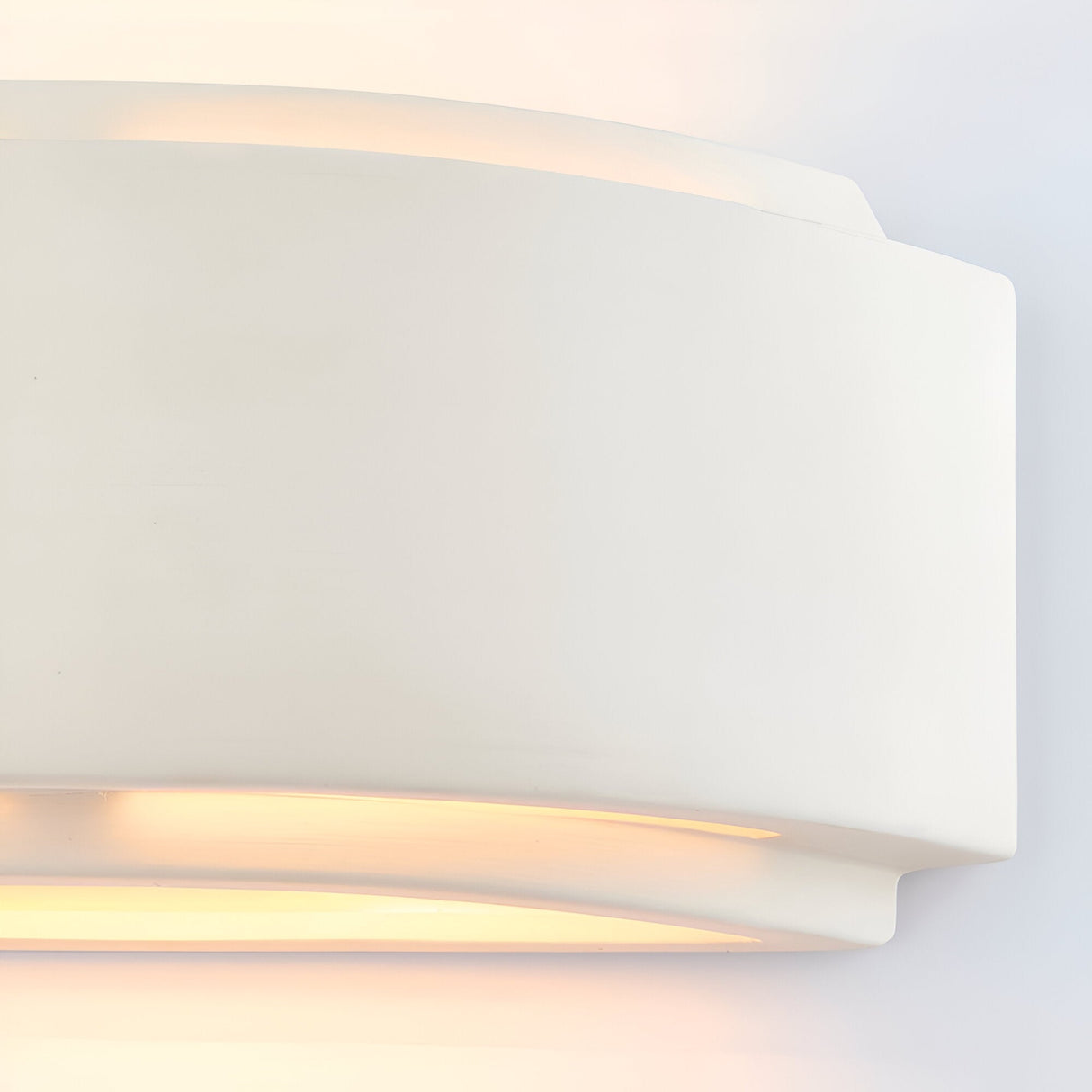 Close-up of the Endon Bramhurst white ceramic wall light showing its curved matt form casting a warm up-and-down glow against a plain wall.