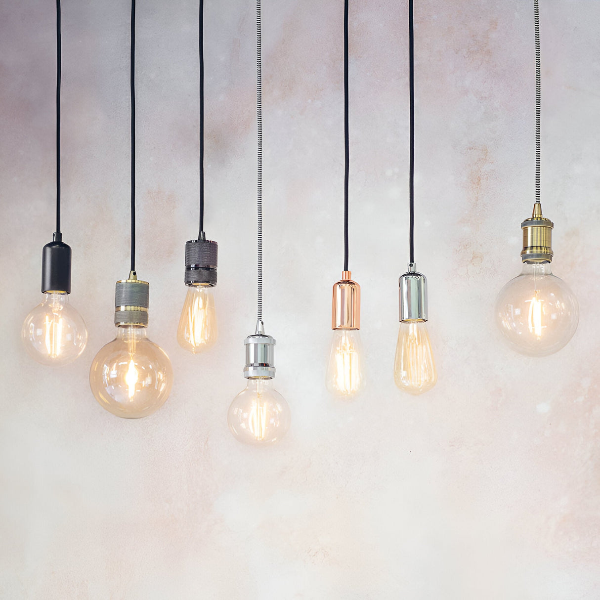 Endon Marlowe pendant lights in black, copper, chrome, brass and concrete finishes hanging with exposed filament bulbs against a neutral wall.