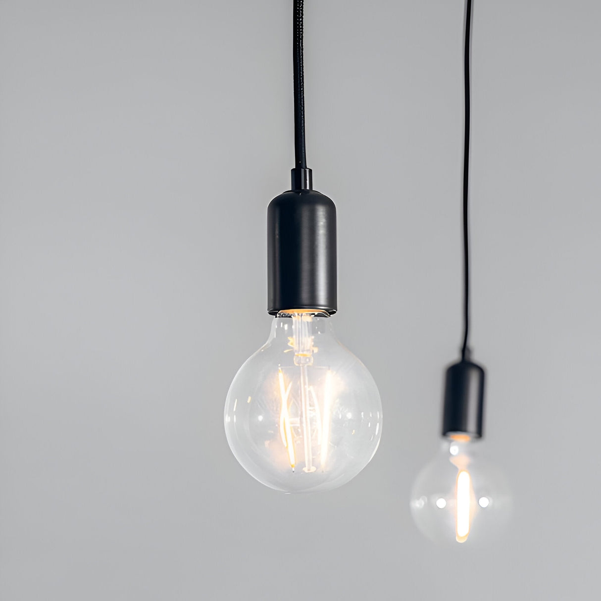 Endon Marlowe pendant lights with two exposed E27 filament bulbs in matt black holders on black fabric flex cables against a light grey background.