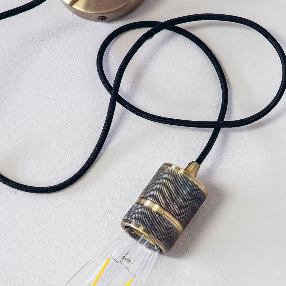 Endon Camden pendant light in antique brass with knurled E27 lamp holder, exposed filament bulb and black braided flex, shown against a light background.