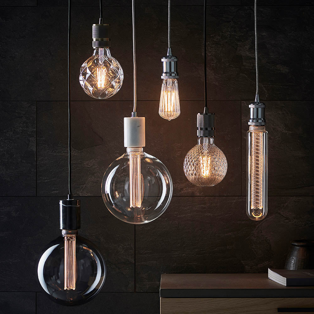 Endon Camden pendant lights clustered over a slate wall with brass and chrome cable fittings and exposed filament LED bulbs in varied globe and tube shapes.