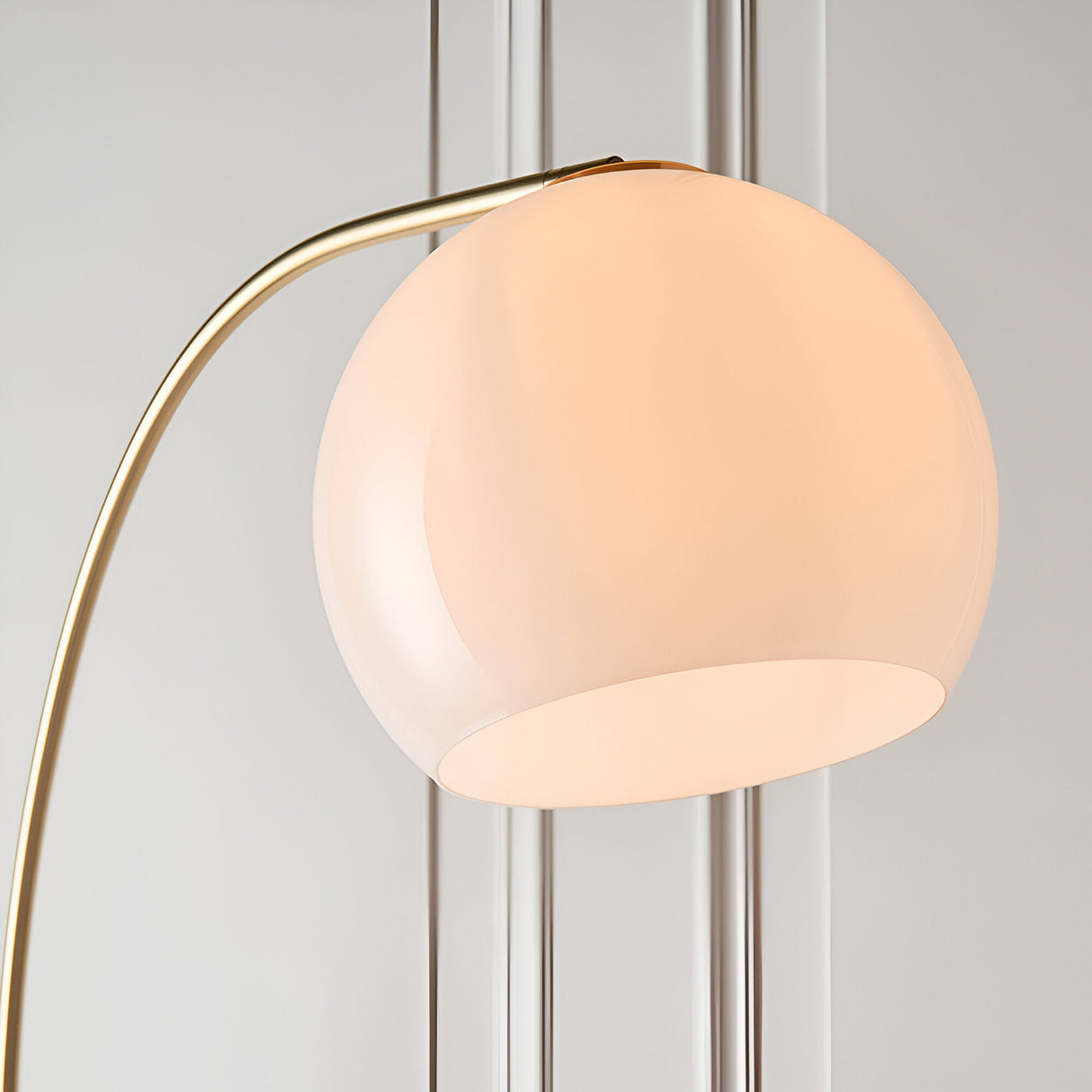 Endon Sinclair floor lamp close-up showing the gloss white glass globe shade angled on a curved brushed brass arm.