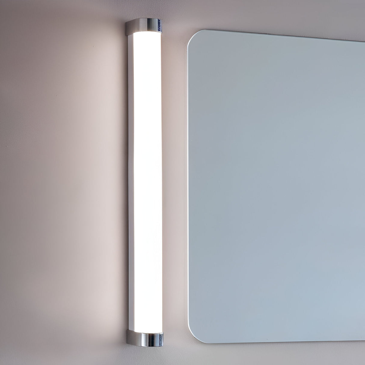 Endon Carlshaw LED large bathroom wall light mounted vertically beside a rounded rectangular mirror, with a slim white ribbed diffuser and chrome end caps.