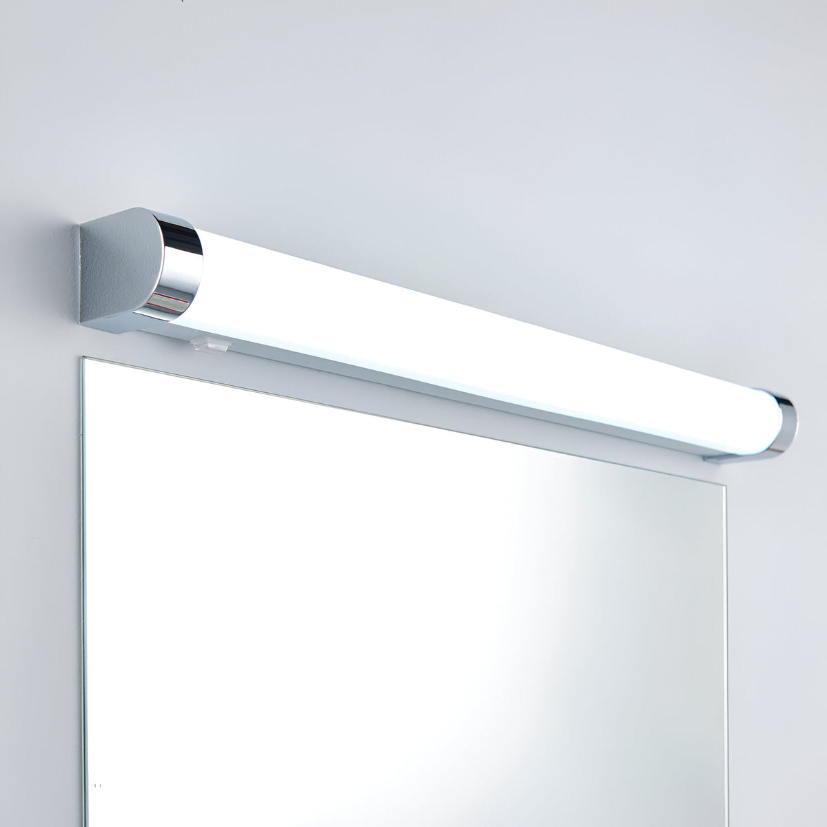 Endon Carlshaw large LED bathroom wall light with slim white ribbed diffuser and chrome ends, mounted above a rectangular mirror on a light wall.