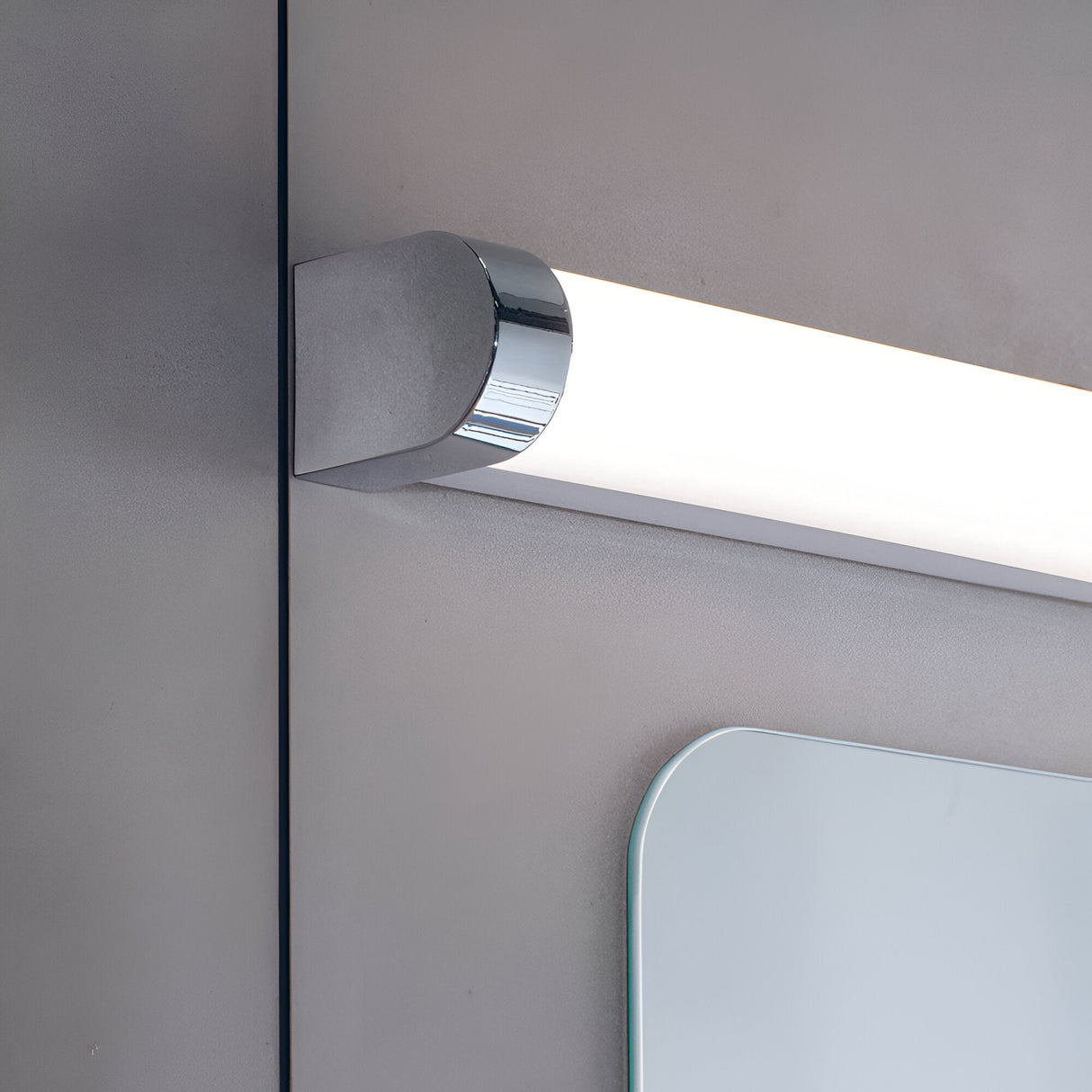 Endon Carlshaw LED bathroom wall light close-up showing the chrome end cap and white ribbed diffuser mounted above a mirror on a light grey wall.