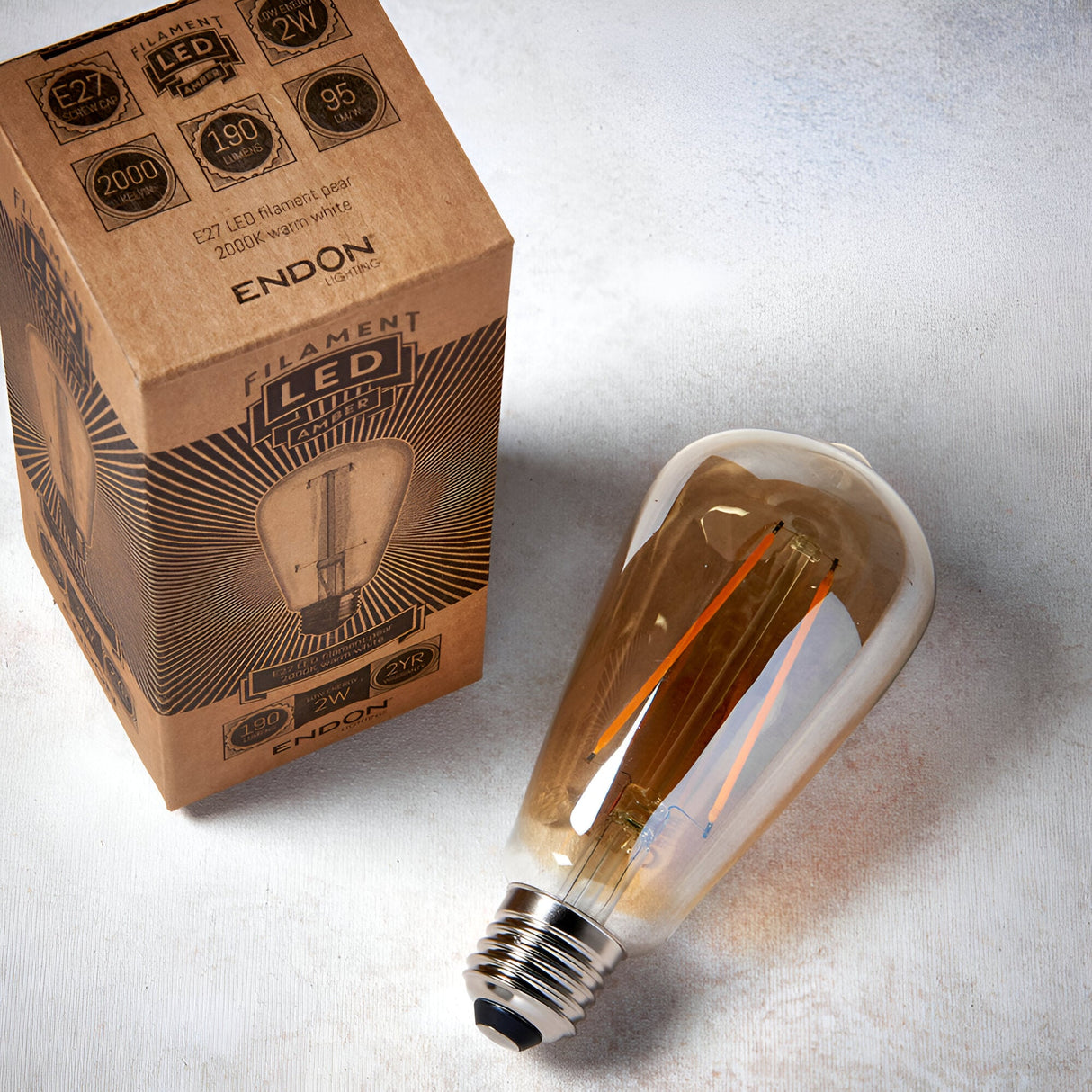 Endon 2W E27 LED filament pear bulb with amber tinted glass and screw cap, shown beside its printed kraft retail box on a light background.