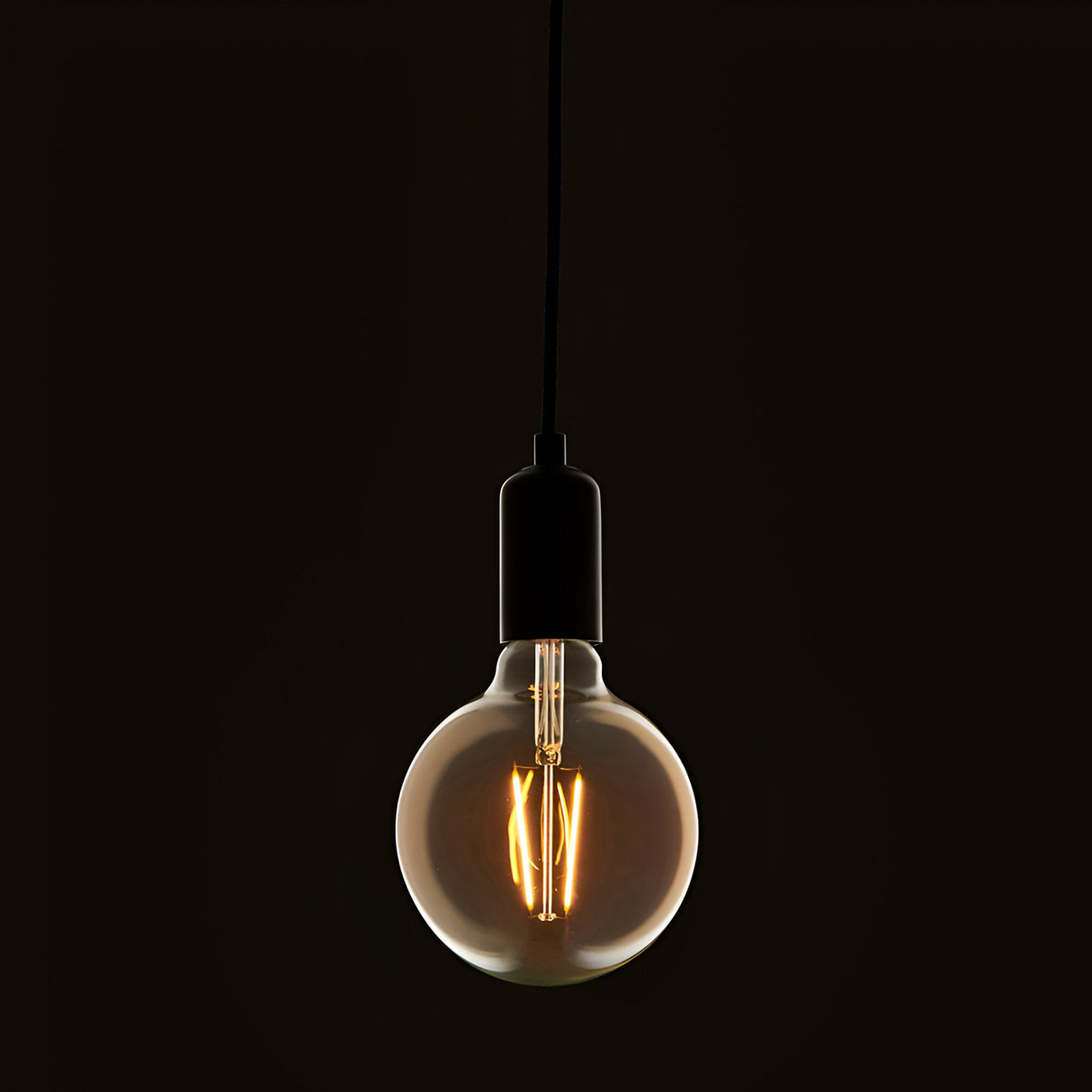 Endon 2W E27 LED filament globe bulb in amber tinted glass, suspended from a black pendant cord with matte black lampholder against a dark background.