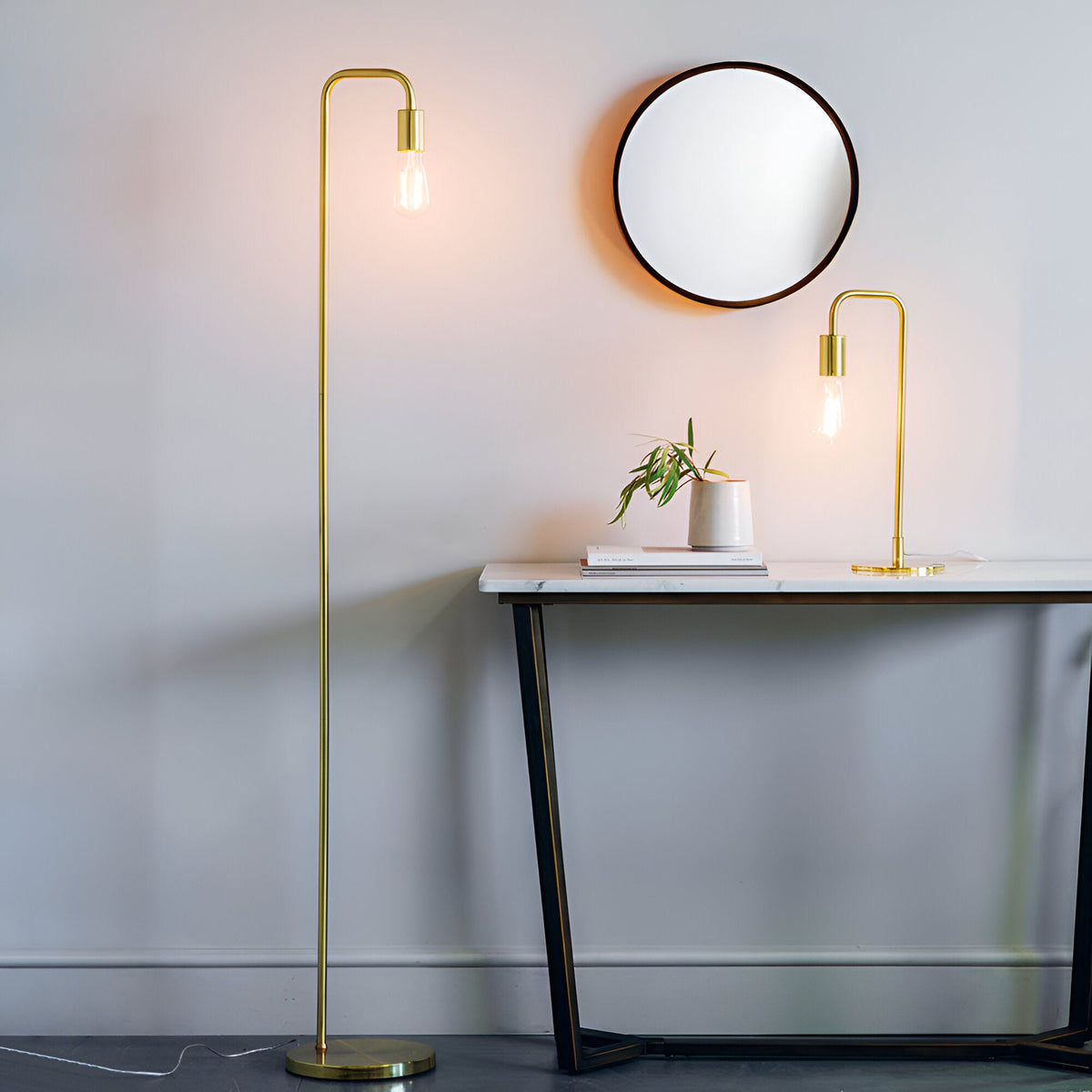 Endon Cliffgrove brushed brass table lamp with exposed filament bulb on a marble console beside a matching floor lamp and round mirror.