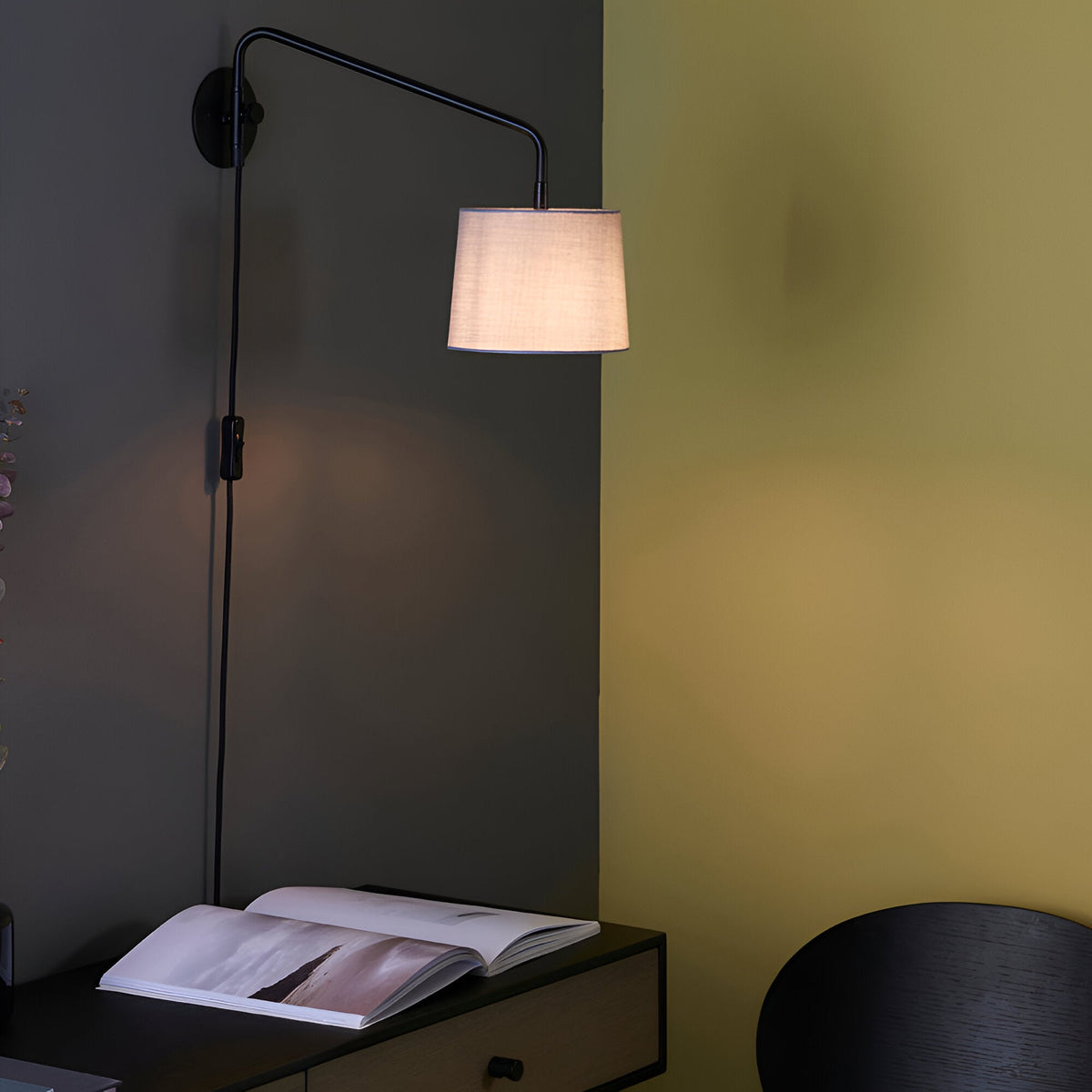 Endon Bevbourne plug-in wall light with matt black swing arm and light grey fabric shade, mounted above a dark desk with an open book.