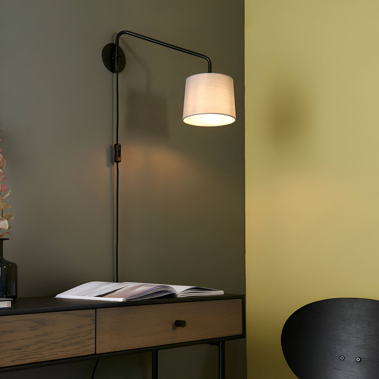 Endon Bevbourne plug-in wall light with matt black swing arm and grey fabric shade, mounted above a wooden console in a bedroom setting.