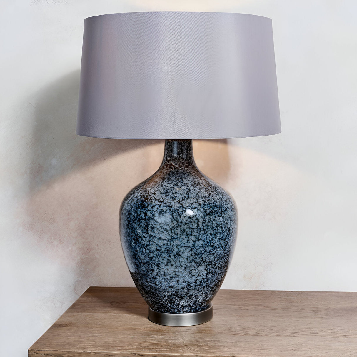 Endon Brenwick table lamp with black speckled glass body, matt nickel base and tapered grey faux silk shade on a wood sideboard.