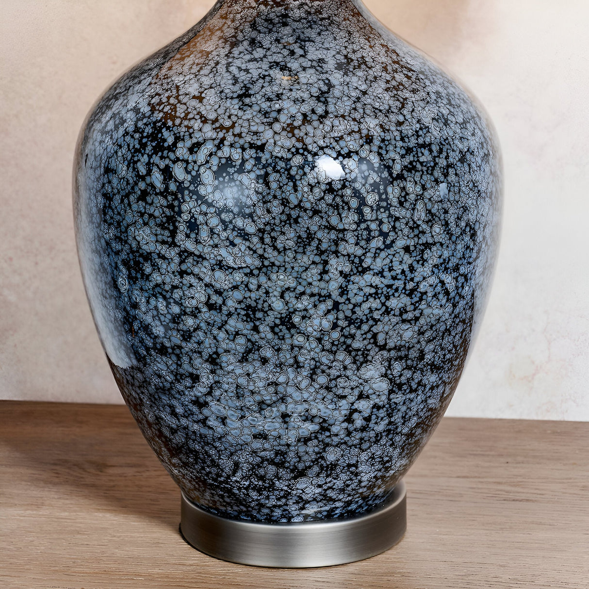 Close-up of the Endon Brenwick table lamp base showing black speckled glass with grey mottling on a brushed nickel foot, set on a wooden surface.