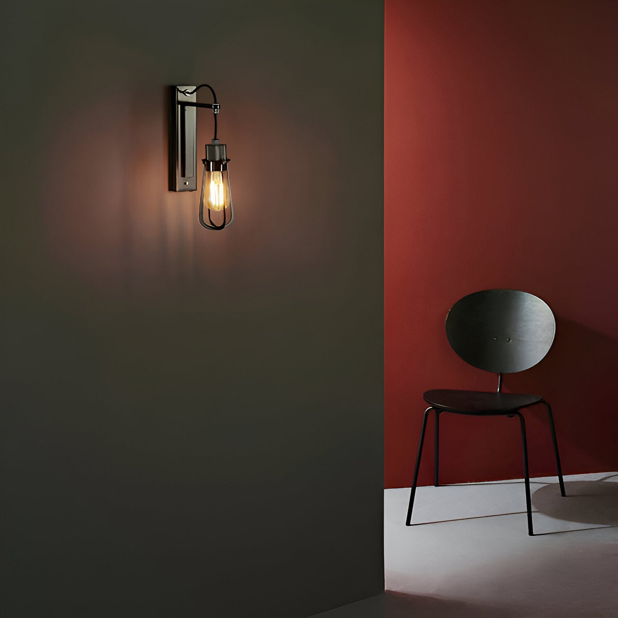 Endon Camden industrial wall light in chrome and black with an exposed E27 filament bulb, mounted on a dark green wall beside a red-walled corner with a chair.
