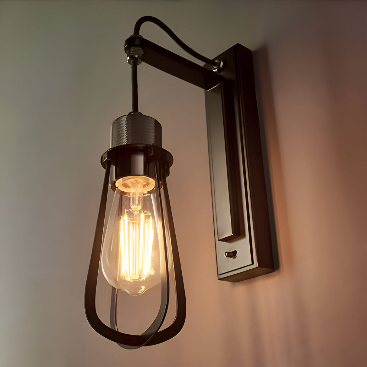 Endon Camden industrial wall light with caged teardrop shade, exposed E27 filament bulb, and chrome and black stepped bracket mounted on a pale wall.