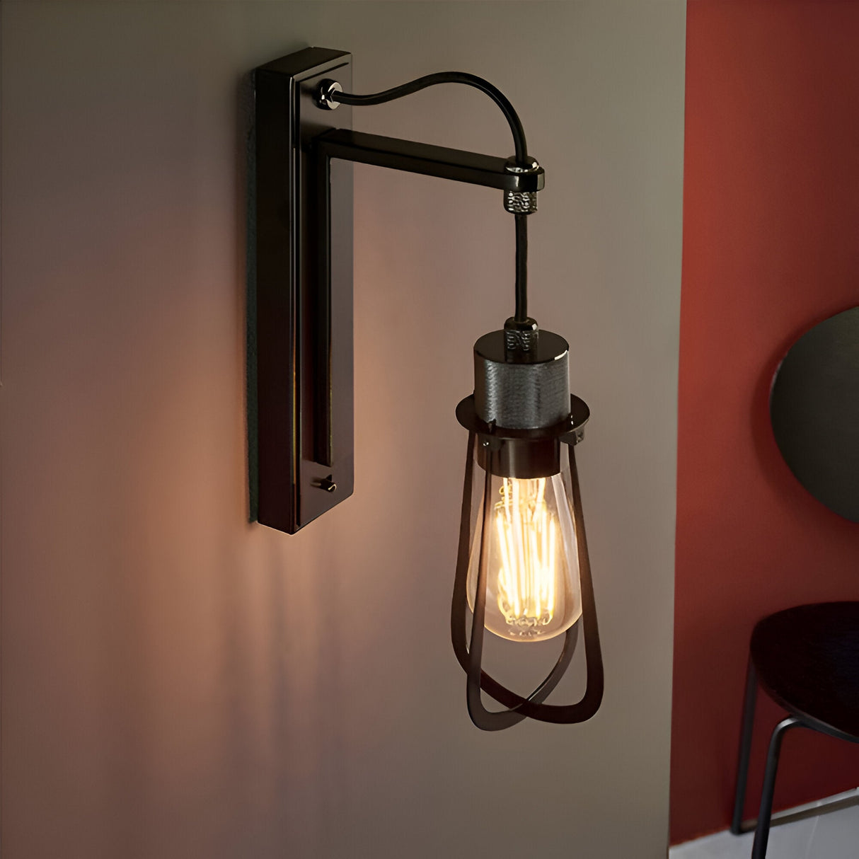 Endon Camden industrial wall light in black chrome with a caged shade and exposed E27 filament bulb, mounted on a wall between grey and red panels.