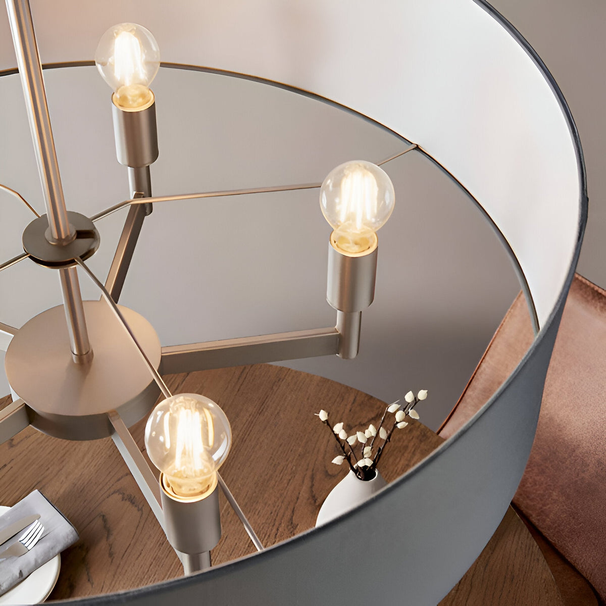 Close-up of Endon Bramstead pendant light interior showing matt nickel arms with E27 lamp holders, exposed bulbs, and grey fabric shade above a wooden table.