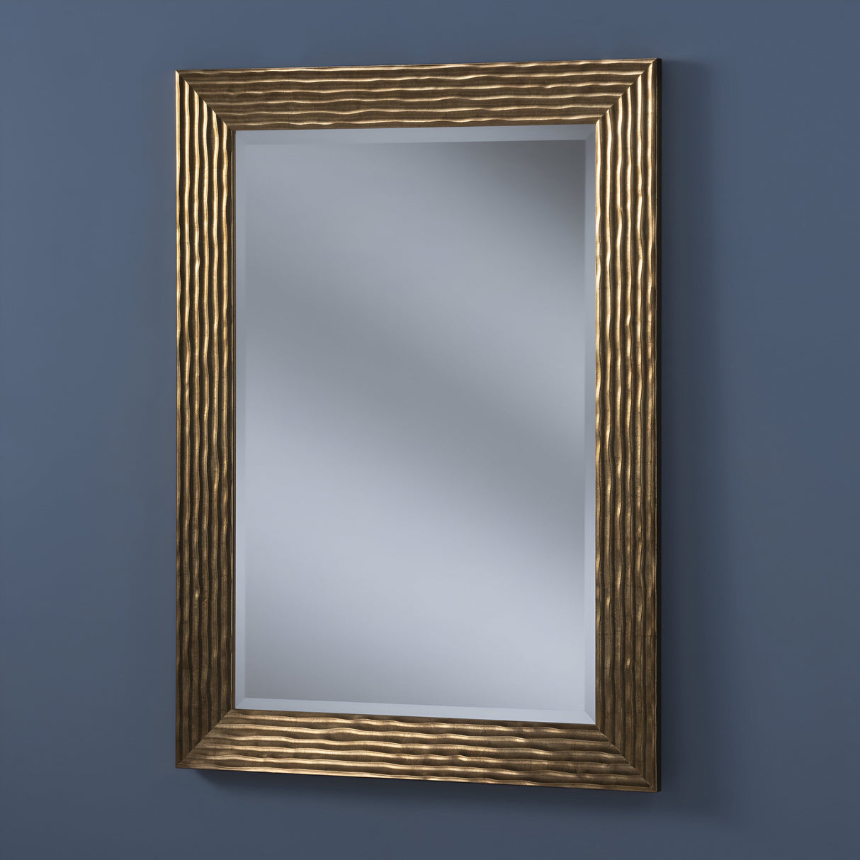 The Venevia Rectangle Wall Mirror - Gold hangs elegantly on a solid blue wall, showcasing its textured frame.
