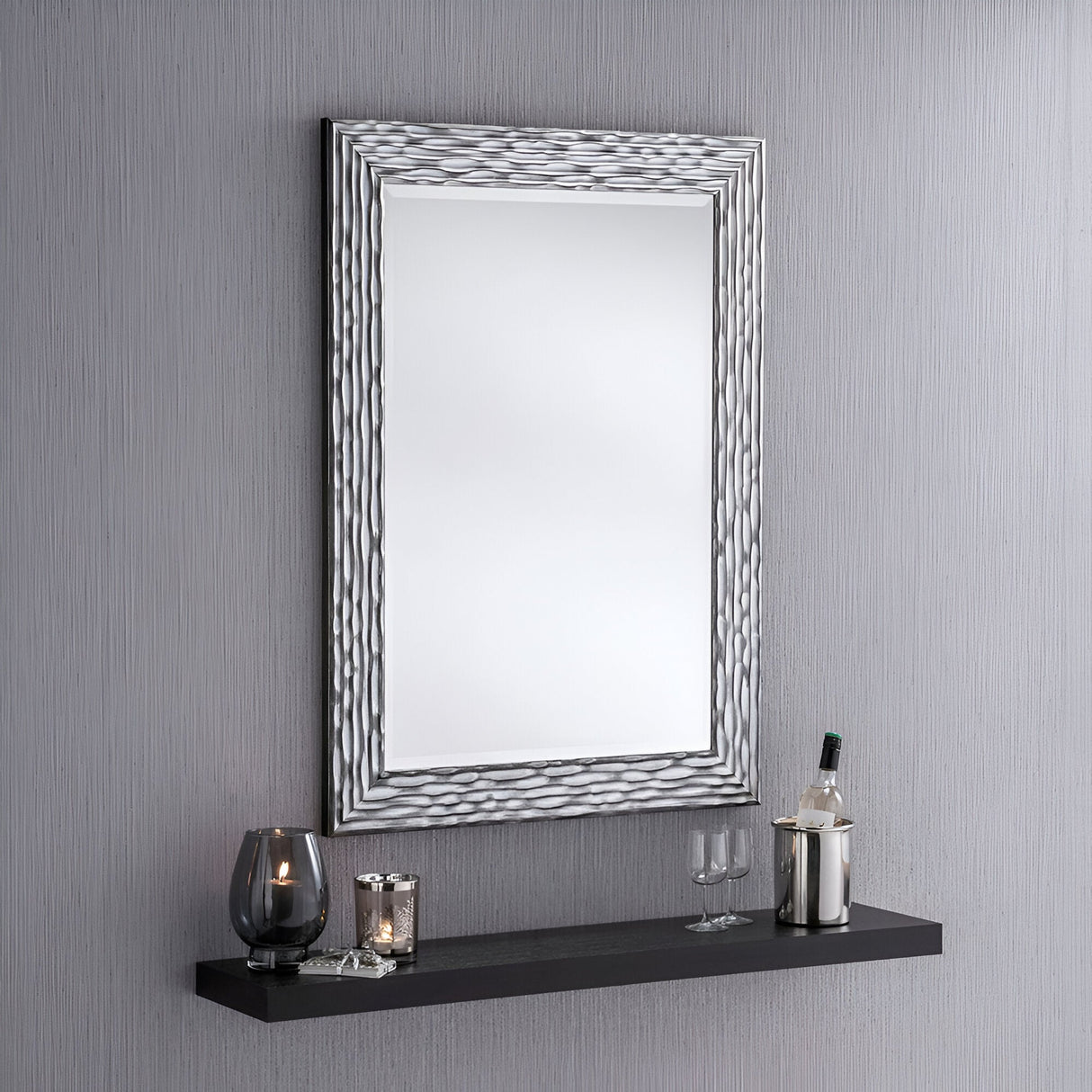The Halo Rectangle Wall Mirror - Black exudes modern elegance as it hangs on a gray wall above a black floating shelf holding two wine glasses, a bottle of wine in a metal holder, a black candle holder, and a decorative candle.