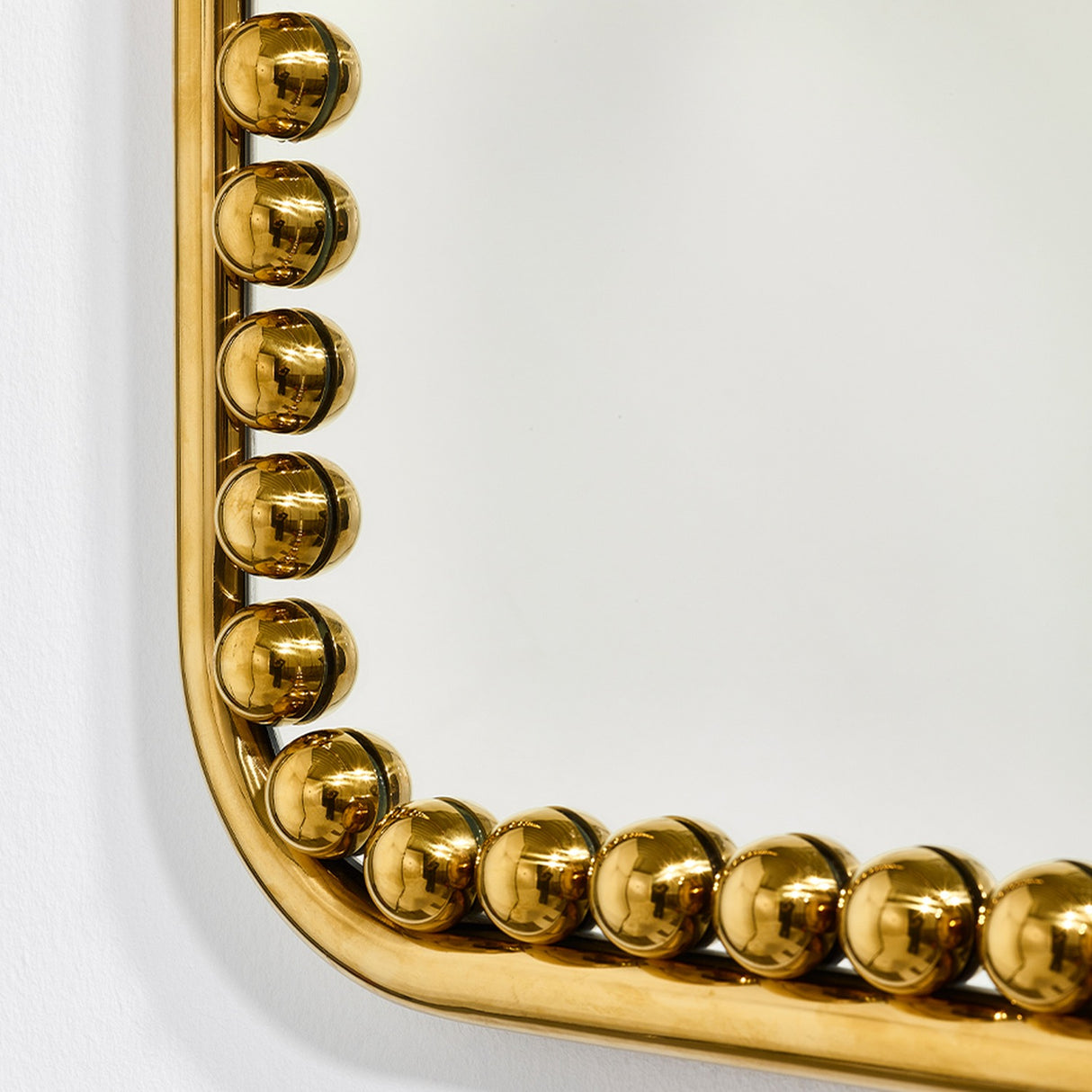 Close-up of the Diva Square wall mirror's corner, showing a gold beaded frame with individual spherical beads around the edge, set against a plain white background.