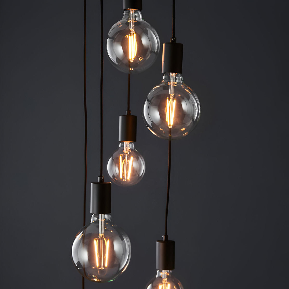 Marlowe 6 Light Pendant in matt black, showing globe bulbs on staggered black fabric flex drops with matt black fittings against a dark background.
