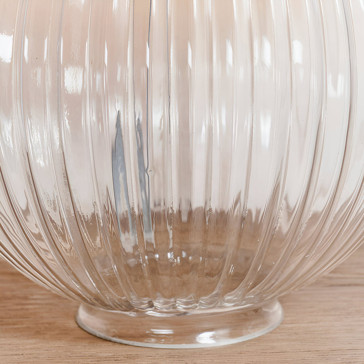 Close-up of the Endon Brockdale table lamp base showing the clear ribbed glass column and clear glass foot on a light wood surface.