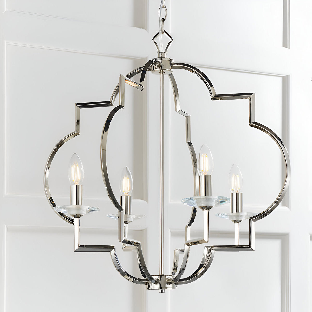 Bramfield 4 Light Pendant in polished nickel with quatrefoil frame, crystal bobeches and candle-style bulbs, hung against a white panelled wall.