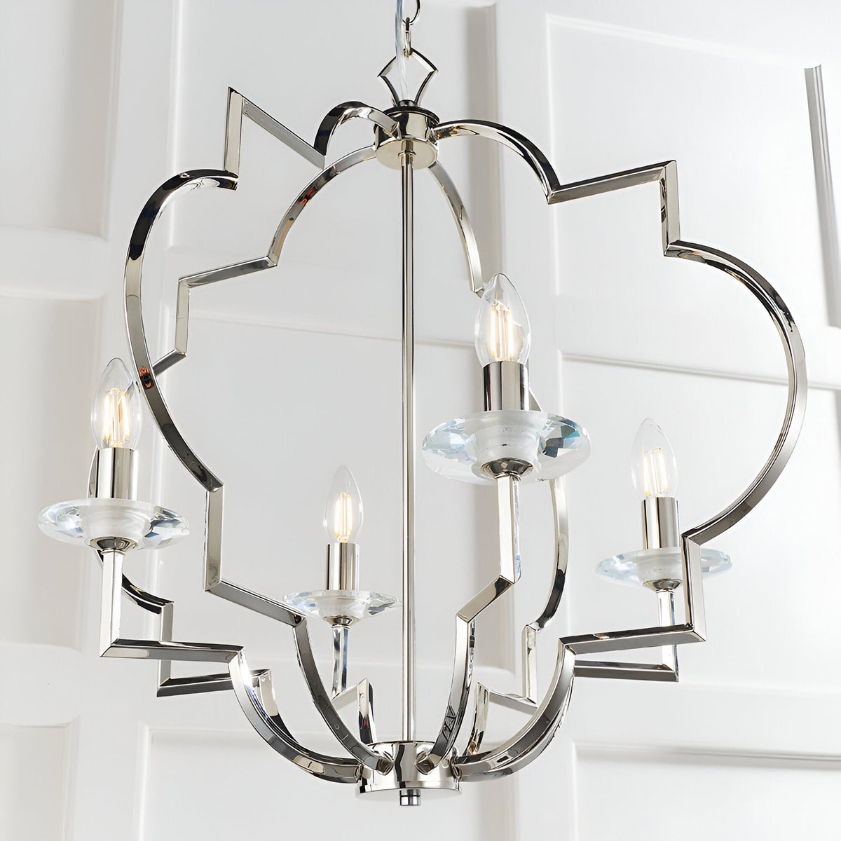 Bramfield 4 Light Pendant in polished nickel with an ornate scrolled frame, crystal glass bobeches, and candle-style bulbs, shown against a white panelled wall.