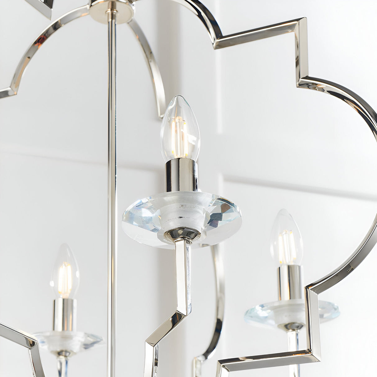 Close-up of the Bramfield 4 Light Pendant in polished nickel with candle bulbs, crystal glass bobeches, and a quatrefoil-shaped frame on a white background.