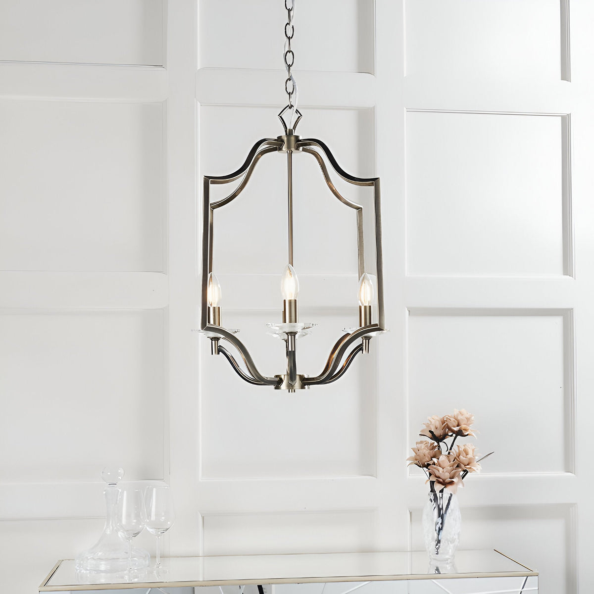 Endon Caldbourne 4 light pendant in antique brass with curved frame and crystal bobeches, hung on chain above a mirrored console in a panelled room.