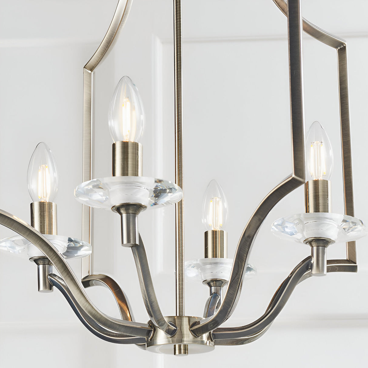 Endon Caldbourne 4 light pendant in antique brass with curved arms, clear K5 crystal bobeches and candle bulbs, shown against a white ceiling.