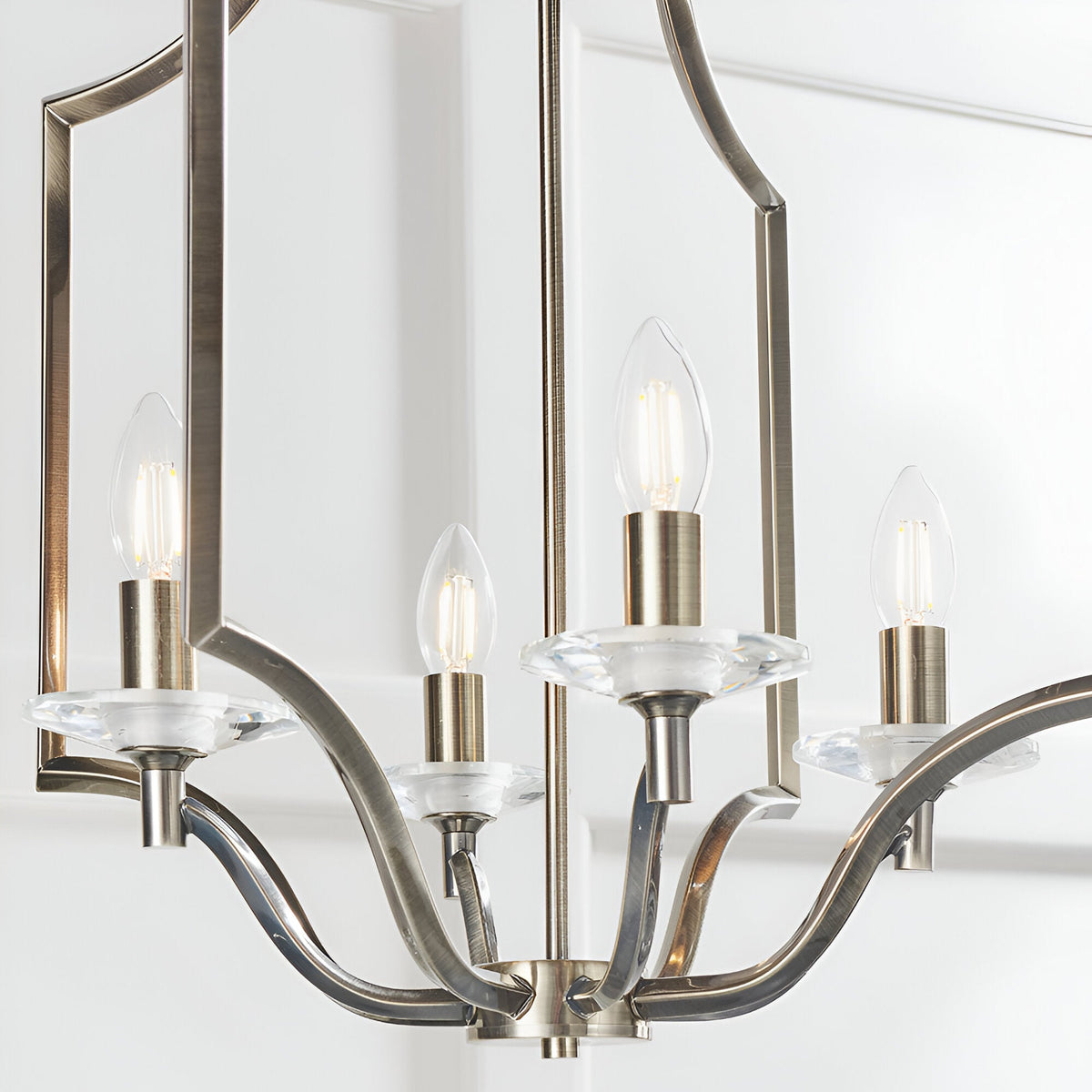 Endon Caldbourne 4 light pendant in antique brass with curved arms, clear K5 crystal bobeches and candle bulbs, shown against a white panelled wall.