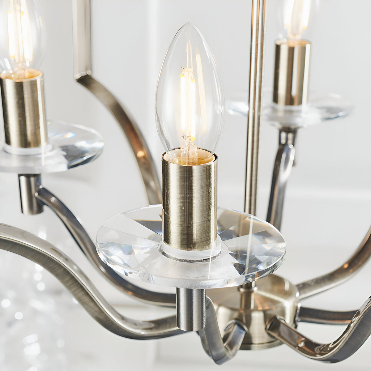 Close-up of Endon Caldbourne 4 light pendant showing antique brass candle-style lampholders with clear K5 crystal bobeches and lit filament bulbs.