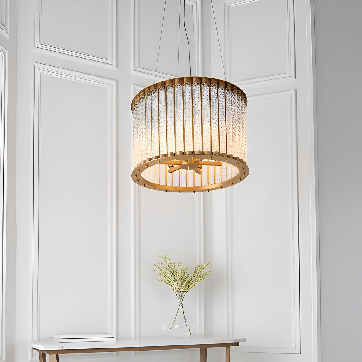 Cliffdale 6 Light Pendant in matt gold, drum-shaped with twisted clear glass rods, hanging above a console table in a panelled white room.