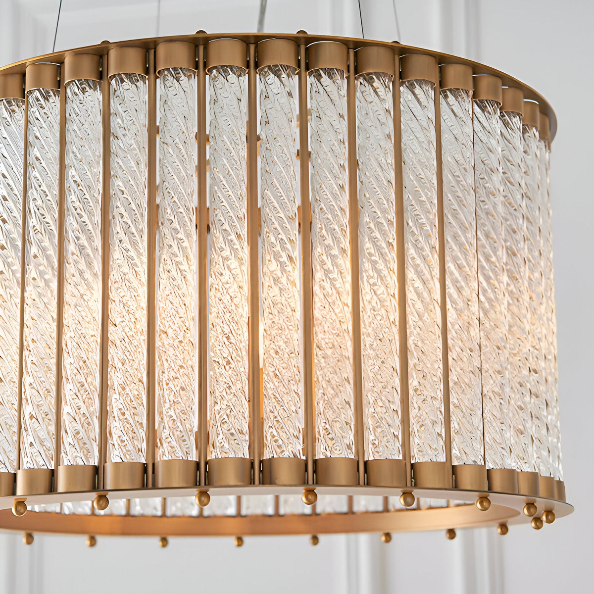 Cliffdale 6 Light Pendant in matt gold, drum-shaped frame with twisted clear glass rods glowing from within, close-up on a white background.