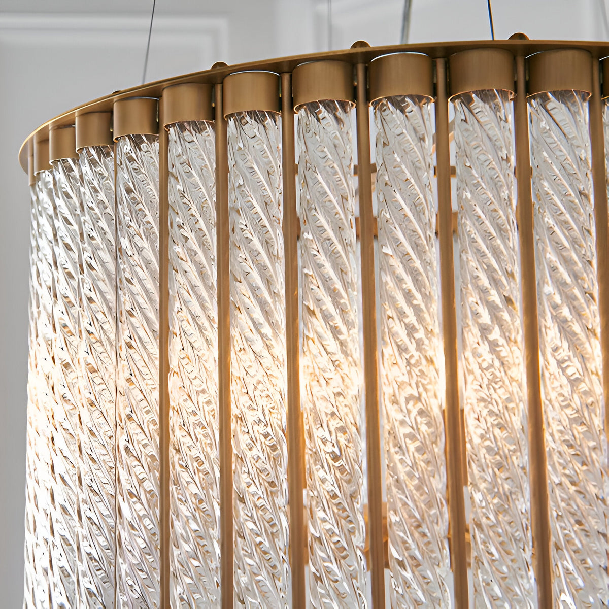 Cliffdale 6 Light Pendant in matt gold, close-up of twisted clear glass rods around a brass frame with glowing warm light inside.