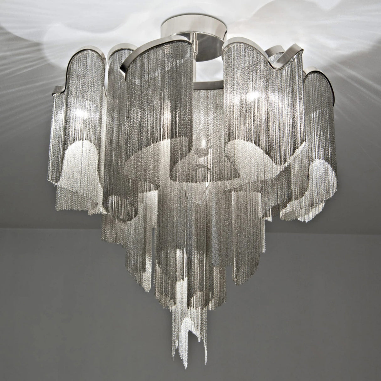 The Valora 8 Light Metal Chain Veil Semi-Flush Ceiling Light in Nickel features cascading chains and wavy edges, creating elegant, dramatic lighting with patterned shadows on ceiling and walls.