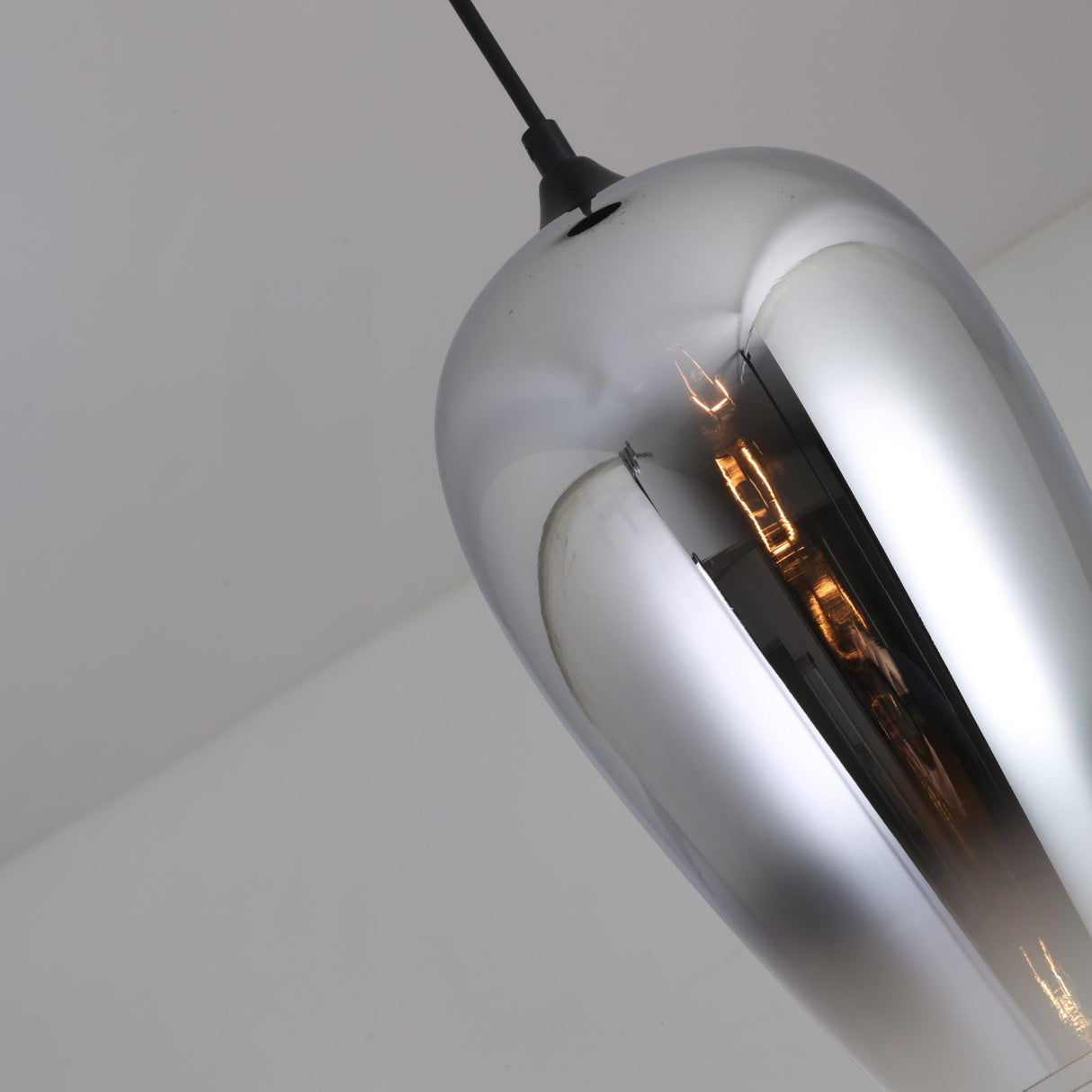 A close-up of the Slice Glass Pendant Light in chrome, showcasing its modern design with a reflective surface and the bulb subtly visible inside as it hangs from the ceiling.