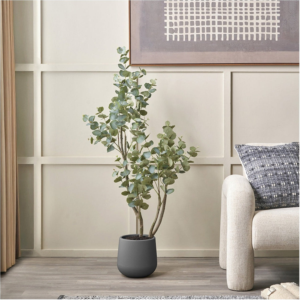 Faux tree in pot, 130cm, with green foliage on multiple stems in a matte grey planter, styled in a living room beside a sofa and framed wall art.